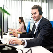 junger Mann telefoniert mit einem Headset vor einem Monitor an einem Schreibtisch
